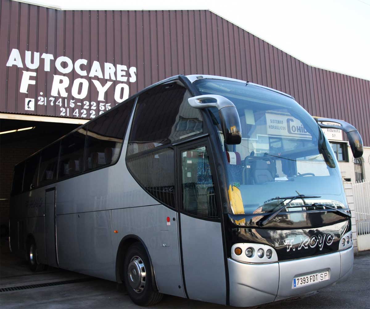 Autobús azul de la empresa "Autocares F. Royo" aparcado en frente de un edificio.